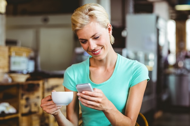 Pretty blonde woman using her smartphone with a cup of coffee