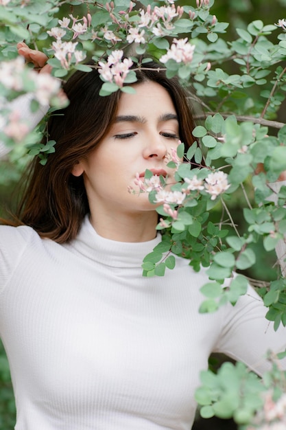 Pretty brunette girl having photoshoot in park smelling tree branch looking down