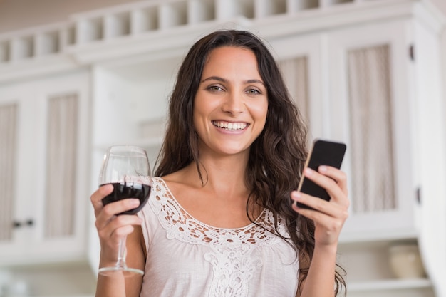 Pretty brunette using smartphone and having glass of wine 