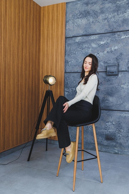 Pretty brunette woman in black pants and brown loafers posing in studio