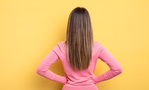 Pretty caucasian woman feeling confused or full or doubts and questions, wondering, with hands on hips, rear view