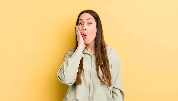 Pretty caucasian woman feeling shocked and astonished holding face to hand in disbelief with mouth wide open