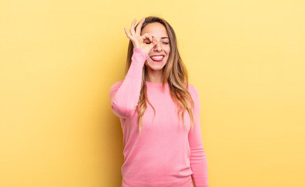 Pretty caucasian woman smiling happily with funny face, joking and looking through peephole, spying on secrets