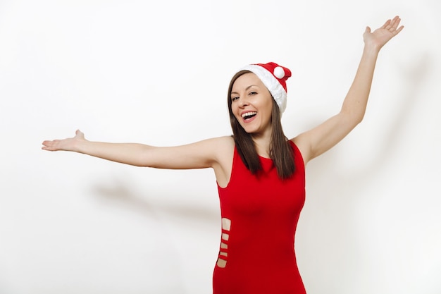 Pretty caucasian young happy woman with charming smile wearing red dress and Christmas hat spreading hands isolated on white background. Santa girl. New Year 2018 holiday. Copy space for advertisement