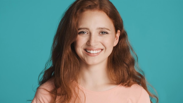 Pretty cheerful redhead girl happily looking in camera over colorful background