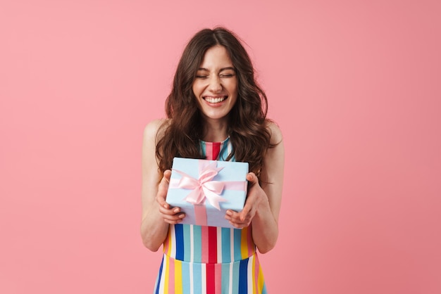 Pretty cheerful smiling positive cute woman posing isolated over pink wall holding present gift box.