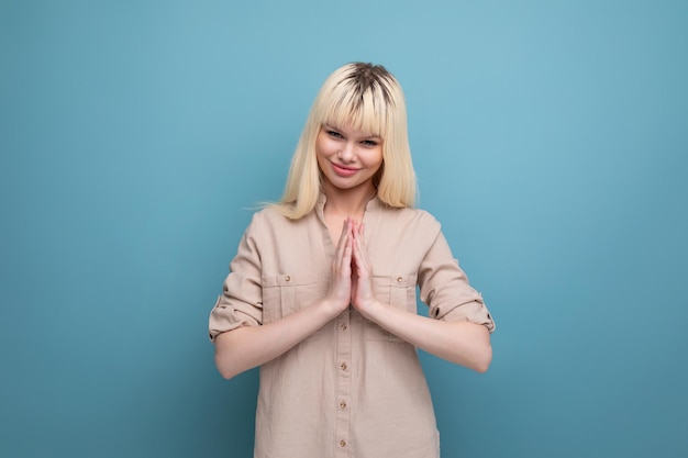 Pretty cheerful young blond woman flirting on blue background with copy space