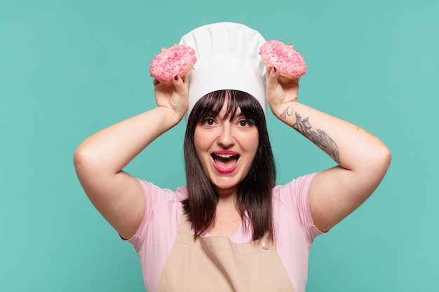 Pretty chef woman surprised expression and holding donuts