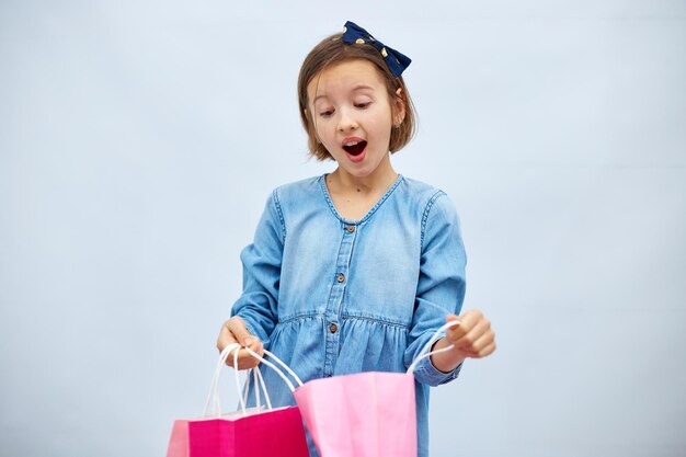 Pretty child girl in casual denim dress hold in hand pink shopping bags