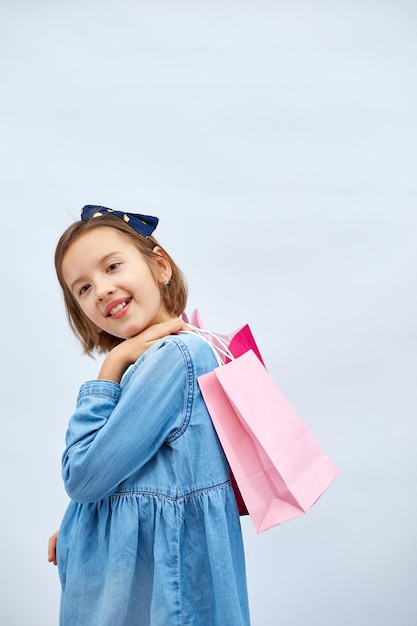 Pretty child girl in casual denim dress hold in hand pink shopping bags