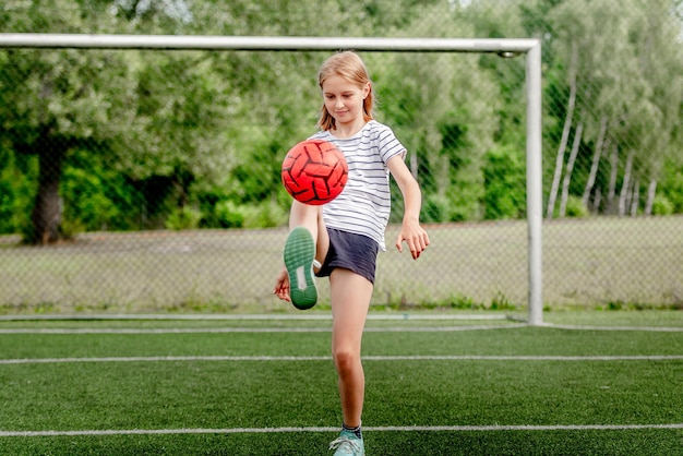 Pretty child girl kicking football ball at socket field cute female kid playing active game