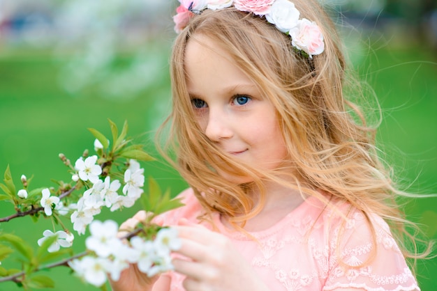 Pretty child girl smiling and playing in flowers of the garden, blooming trees, cherry, apples.