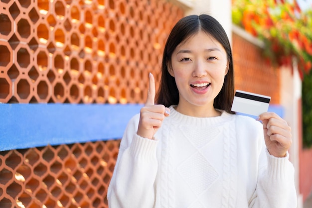 Pretty Chinese woman holding a credit card at outdoors pointing up a great idea