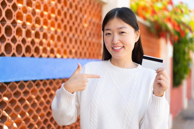 Pretty Chinese woman holding a credit card at outdoors with surprise facial expression