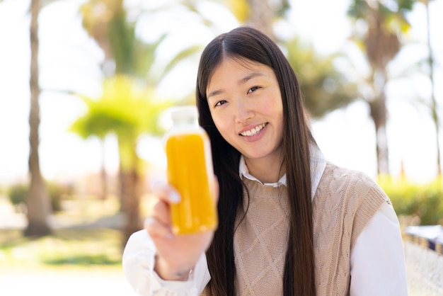 Pretty Chinese woman holding an orange juice at outdoors with happy expression