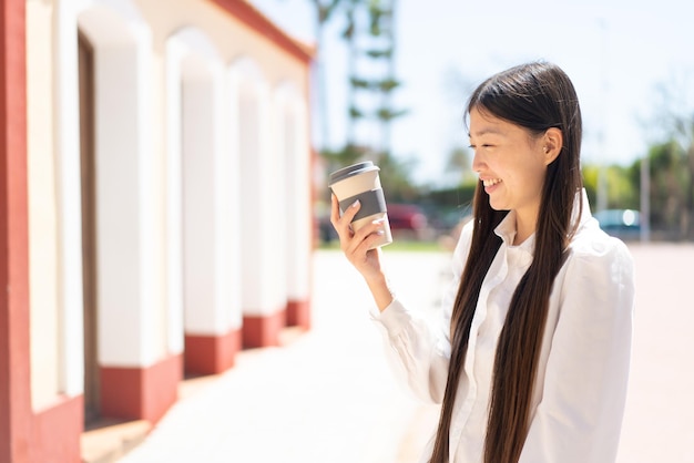 Pretty Chinese woman holding a take away coffee at outdoors with happy expression