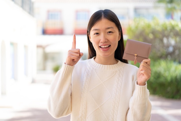 Pretty Chinese woman holding a wallet at outdoors pointing up a great idea