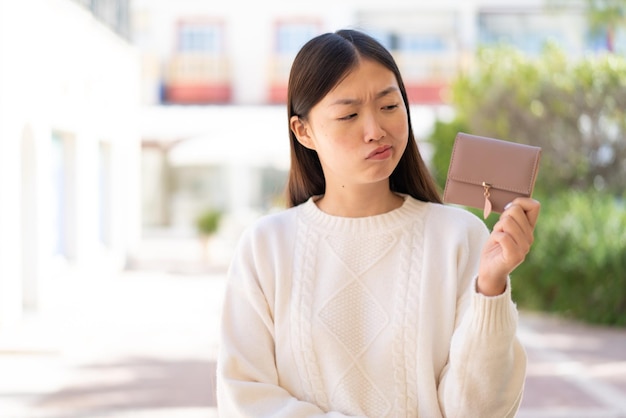 Pretty Chinese woman holding a wallet at outdoors with sad expression