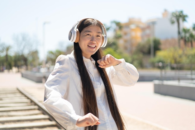 Pretty Chinese woman listening music with headphones at outdoors