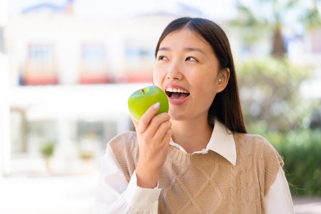 Pretty Chinese woman at outdoors holding an apple with happy expression