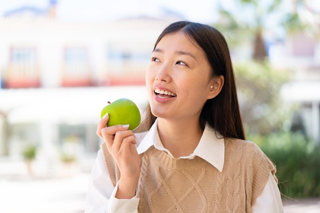 Pretty Chinese woman at outdoors holding an apple with happy expression