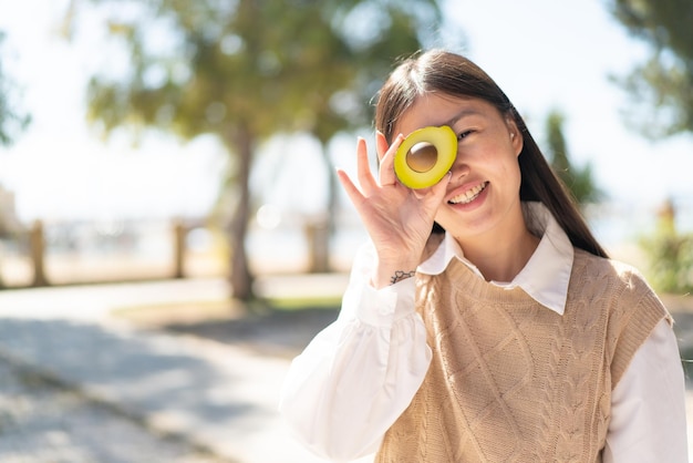 Pretty Chinese woman at outdoors holding an avocado with happy expression