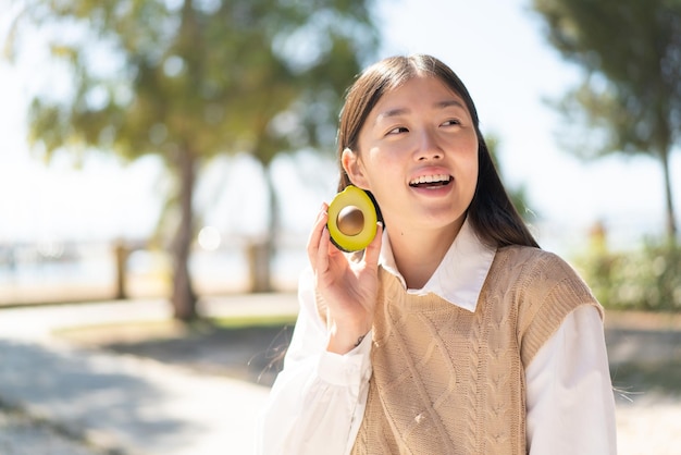 Pretty Chinese woman at outdoors holding an avocado with happy expression