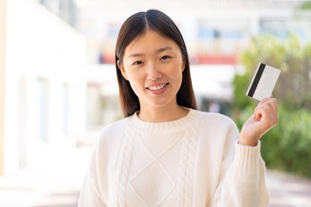 Pretty Chinese woman at outdoors holding a credit card with happy expression