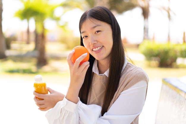 Pretty Chinese woman at outdoors holding an orange and an orange juice