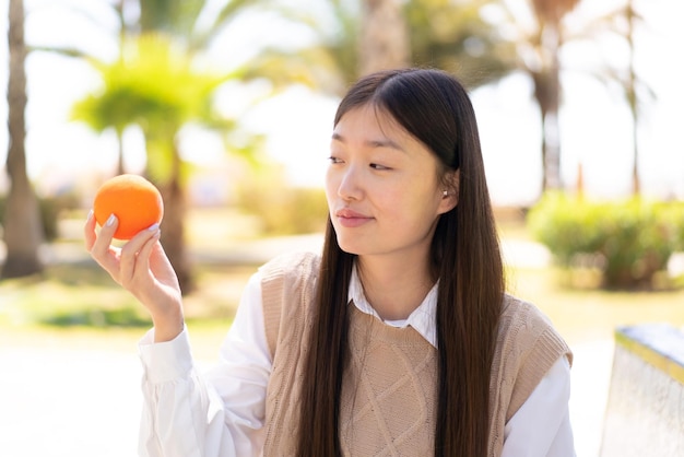 Pretty Chinese woman at outdoors holding an orange