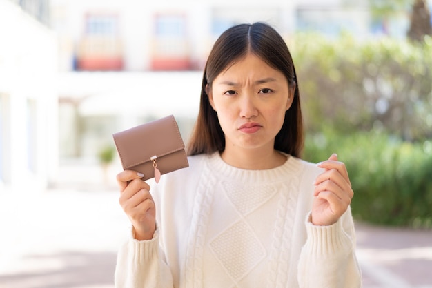 Pretty Chinese woman at outdoors holding a wallet and with sad expression