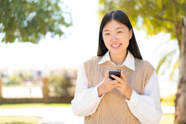 Pretty Chinese woman at outdoors sending a message with the mobile