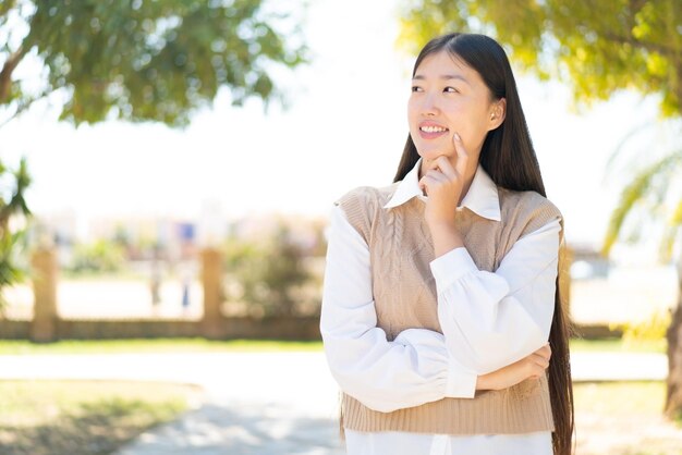 Pretty Chinese woman at outdoors thinking an idea while looking up