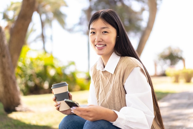 Pretty Chinese woman at outdoors using mobile phone and holding a take away coffee