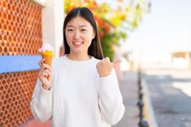 Pretty Chinese woman with a cornet ice cream at outdoors pointing to the side to present a product