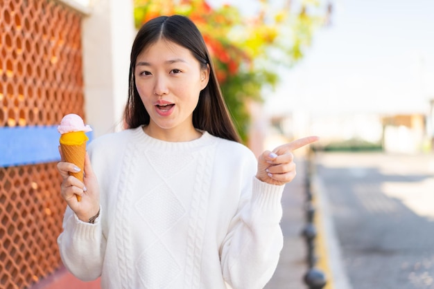 Pretty Chinese woman with a cornet ice cream at outdoors surprised and pointing side