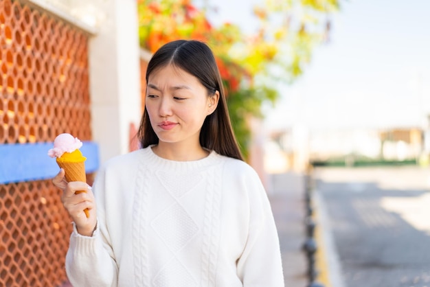 Pretty Chinese woman with a cornet ice cream at outdoors with sad expression