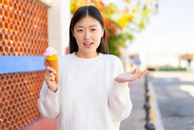 Pretty Chinese woman with a cornet ice cream at outdoors with shocked facial expression