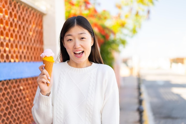 Pretty Chinese woman with a cornet ice cream at outdoors with surprise and shocked facial expression