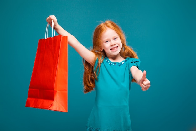 Pretty, cute little girl in blue clothes with long red hair cares package