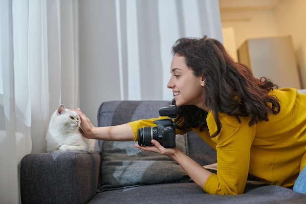 Pretty darkhaired woman with camera stroking her white cat