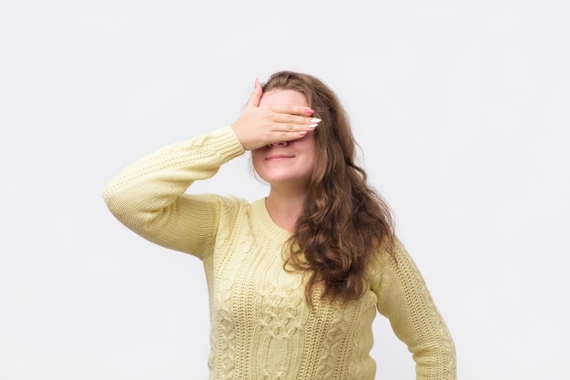 Pretty european girl in yellow sweater closing her eyes with hand having happy expression