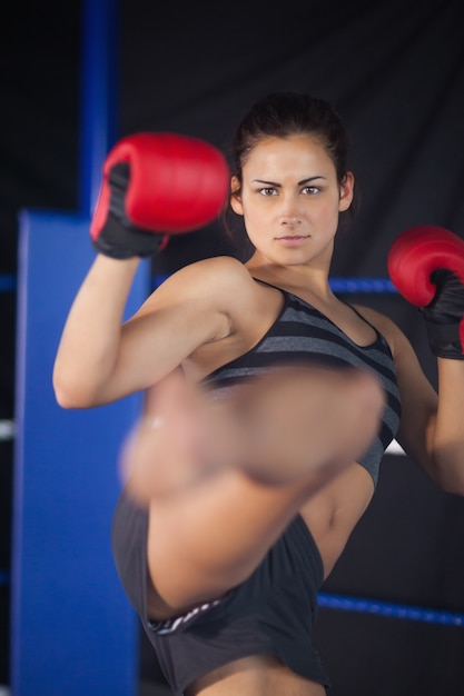 Pretty female boxer performing an air kick in the ring