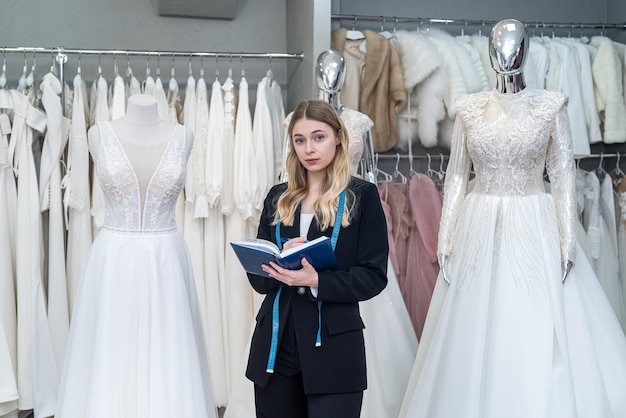 Pretty female designer or seller making notes near dress in wedding fashion store