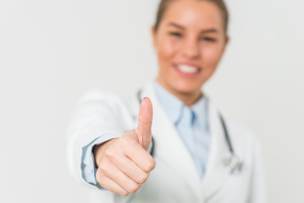 Pretty female doctor with positive gesture by the white wall