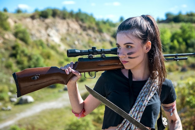 Pretty female hunter in top in forest with weapon in nature