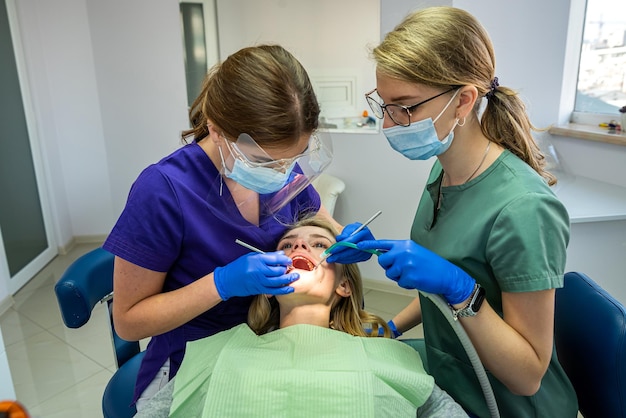 Pretty female patient sitting in armchair while doctor with assistant examining her teeth