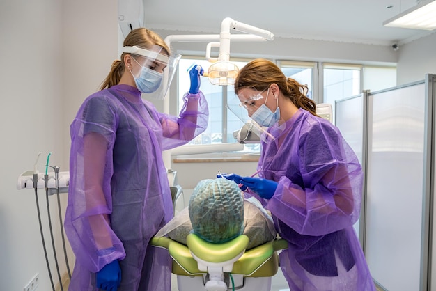 Pretty female patient sitting in armchair while doctor with assistant examining her teeth