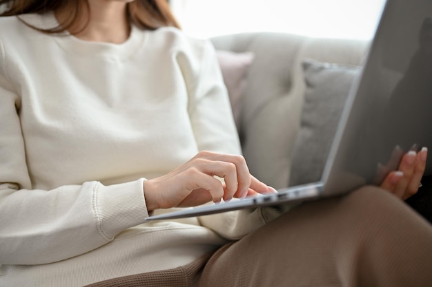 A pretty female sits on a comfy sofa in the living room using laptop computer cropped image