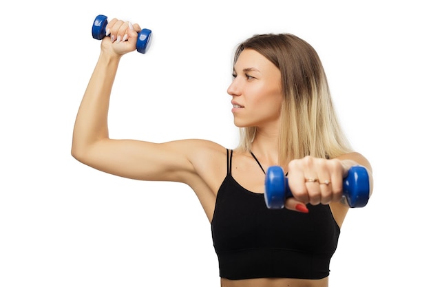 Pretty fit young woman working out with a pair of dumbbells standing sideways to show off her shapely figure while looking at the camera with a smile isolated on white